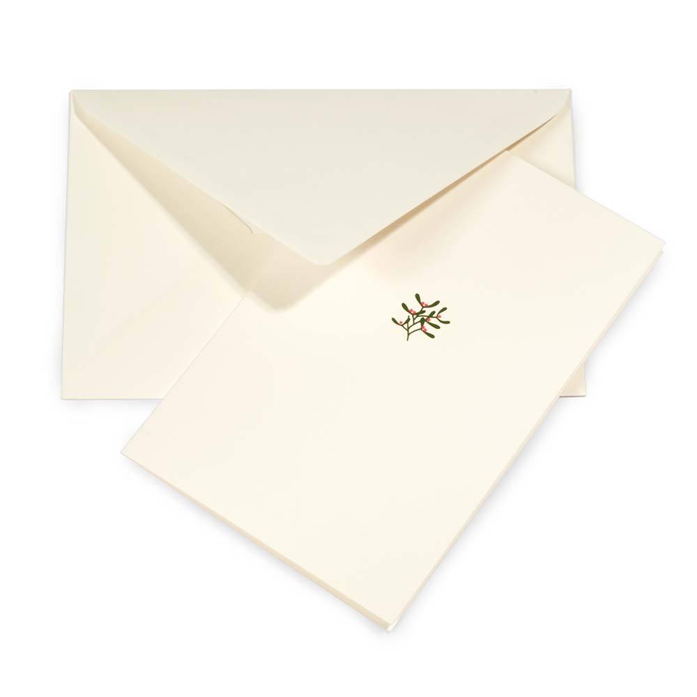 A cream-colored Christmas card with a small mistletoe sprig of olive leaves and pink berries in the center, shown with a matching cream envelope.