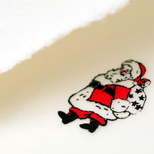A close-up of a cream-colored Christmas card with deckled edges, featuring a small illustration of Santa Claus in a red suit holding a sack of gifts.