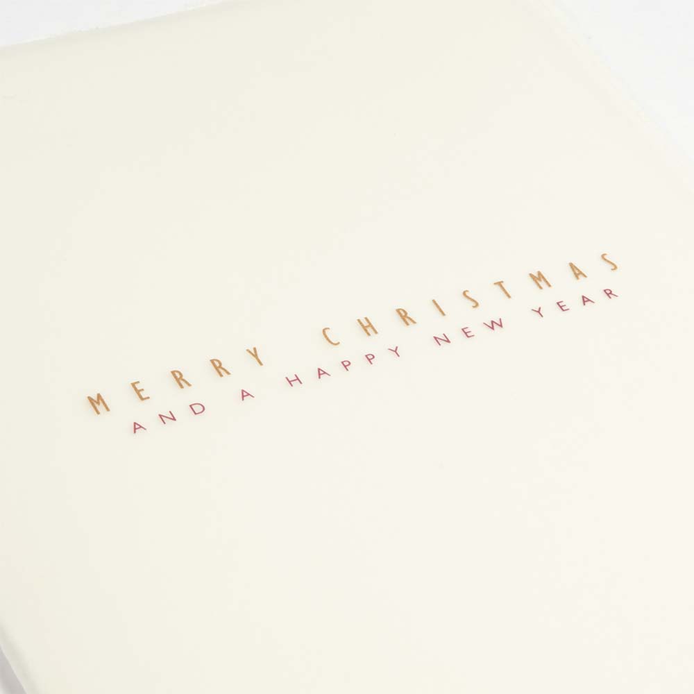 Close-up of a minimalist Christmas card made from textured cream deckle-edged paper, featuring delicate gold lettering that reads “Merry Christmas and Happy New Year".