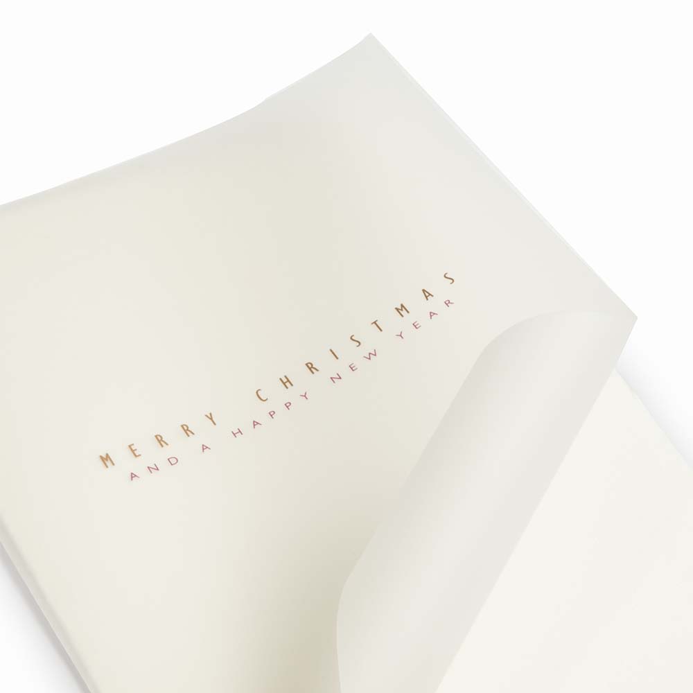 Close-up of a minimalist Christmas card made from textured cream deckle-edged paper, featuring delicate gold lettering that reads “Merry Christmas and Happy New Year".