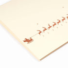 A close-up of a minimalist cream-colored Christmas card showing a row of small gold reindeer pulling a sleigh, numbered up to 31. The reindeer on the 24th is marked in red. Paired with a matching cream envelope.