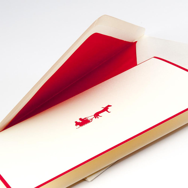 Cream-colored Christmas card with red border, showing a red silhouette of Santa in a sleigh pulled by one reindeer, paired with an envelope lined in bright red.