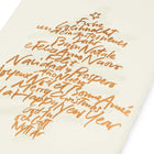 Close-up of a cream-colored Christmas card with deckled edges, featuring a gold handwritten text design arranged in the shape of a Christmas tree with a small star on top.