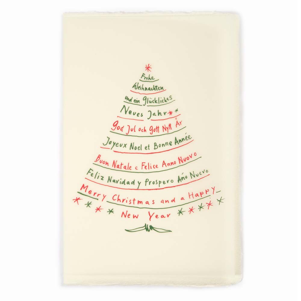 A cream-colored Christmas card with deckled edges, featuring festive greetings in multiple languages written in red and green text arranged in the shape of a Christmas tree.