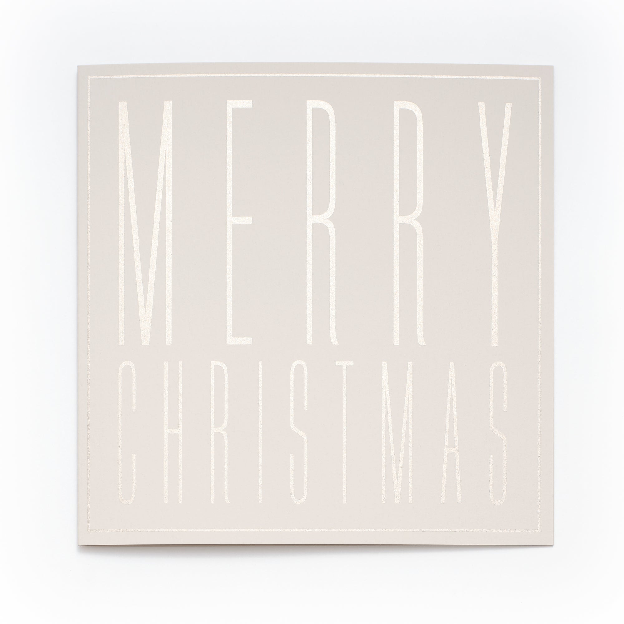 A square cream-colored Christmas card with embossed tall block letters spelling "MERRY CHRISTMAS".