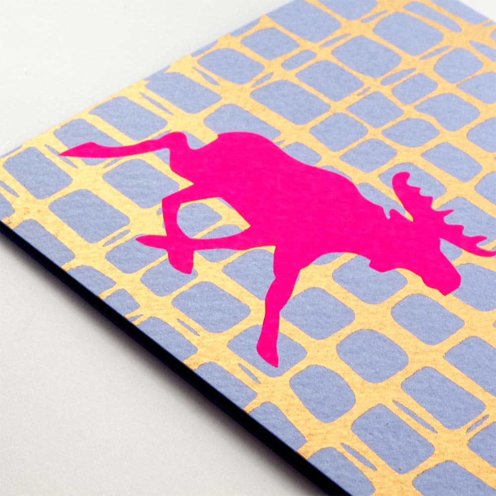 A close-up of a modern Christmas card with a bright pink moose silhouette against a blue and gold grid-like background.