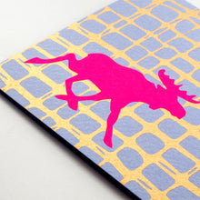 A close-up of a modern Christmas card with a bright pink moose silhouette against a blue and gold grid-like background.