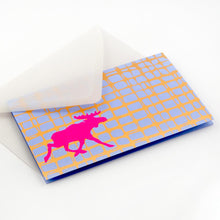 Modern Christmas card with a bright pink moose silhouette against a blue and gold grid-like background, paired with a translucent white envelope.
