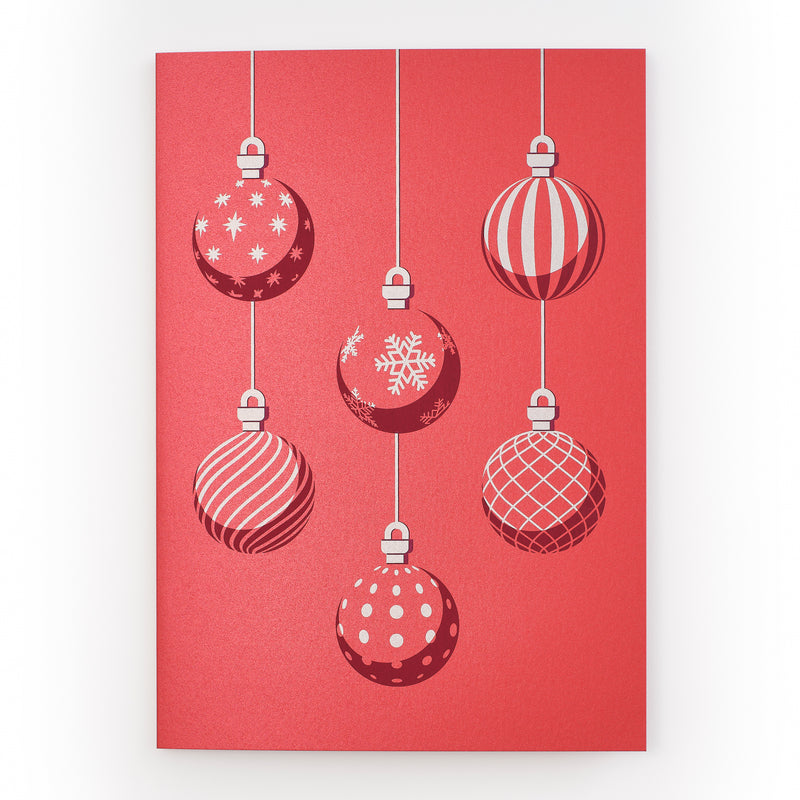 A red Christmas card featuring six hanging ornaments in white and red with various patterns including stripes, snowflakes, and polka dots.