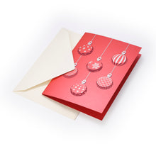 A red Christmas card featuring six hanging ornaments in white and red with various patterns including stripes, snowflakes, and polka dots, shown with a cream-colored envelope.