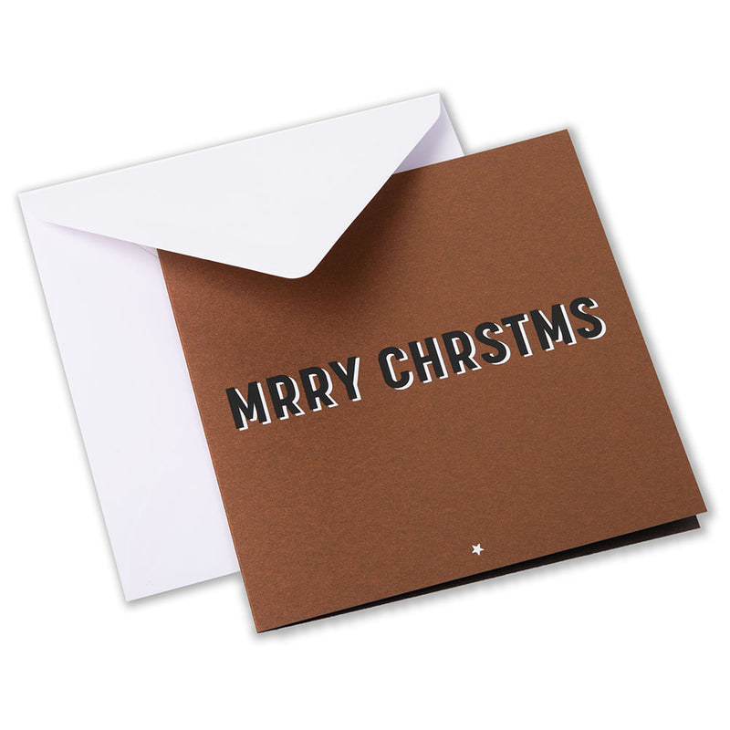 Brown Christmas card with bold black and white shadow text spelling “MRRY CHRSTMS” in a playful, minimalist font, paired with a plain white envelope.
